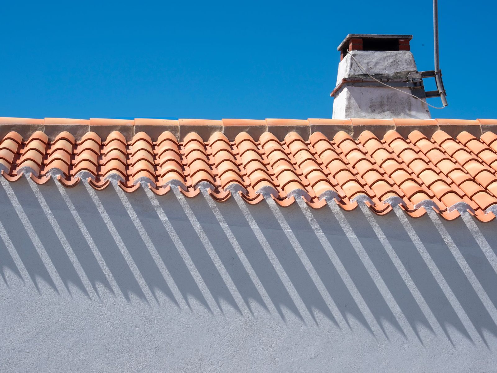 Clay tile roof edge above a white wall, with a chimney